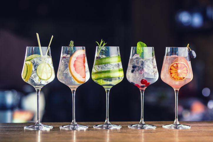 Five colorful gin tonic cocktails in wine glasses on bar counter in pup or restaurant.